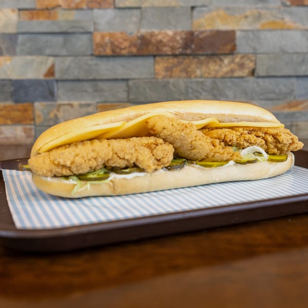 A Megawich sandwich with crispy chicken, pickles, and cheese on a striped paper-lined tray.