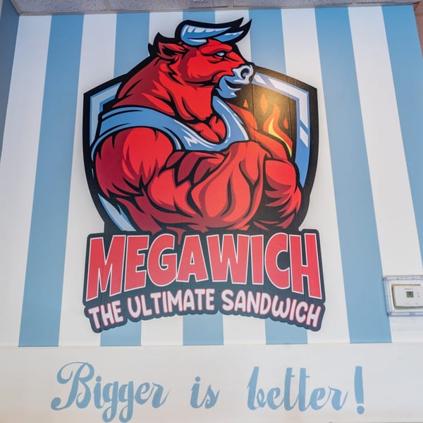 Megawich logo featuring a muscular red bull with blue horns and a shield, on a striped wall.