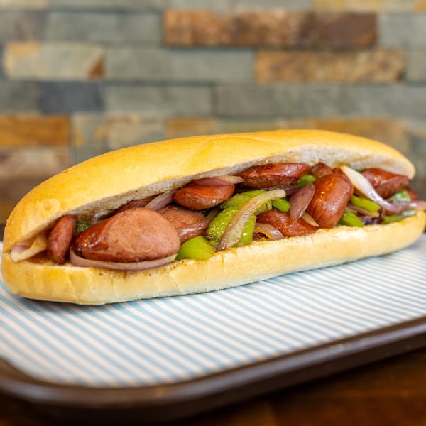 A Megawich sandwich filled with sliced sausage, green peppers, and red onions on a striped paper.