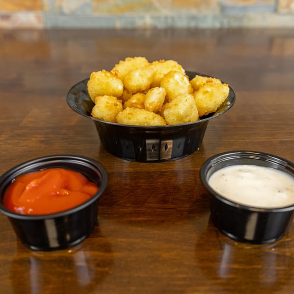 A black bowl of golden-brown cheese curds with small containers of ketchup and ranch dressing.