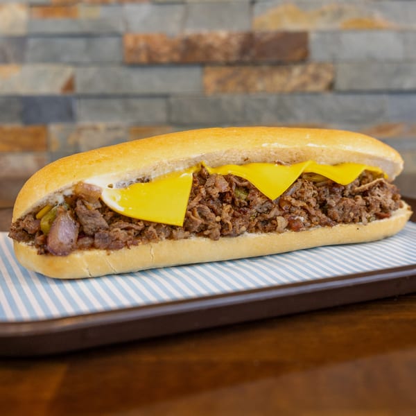 A Megawich cheesesteak sandwich with melted cheese, steak, and onions on a striped paper-lined tray.
